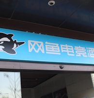 A building entrance features a vibrant blue sign with white Chinese characters and a stylized orca logo in black and white. The overall appearance suggests an establishment focused on eSports or digital activities.